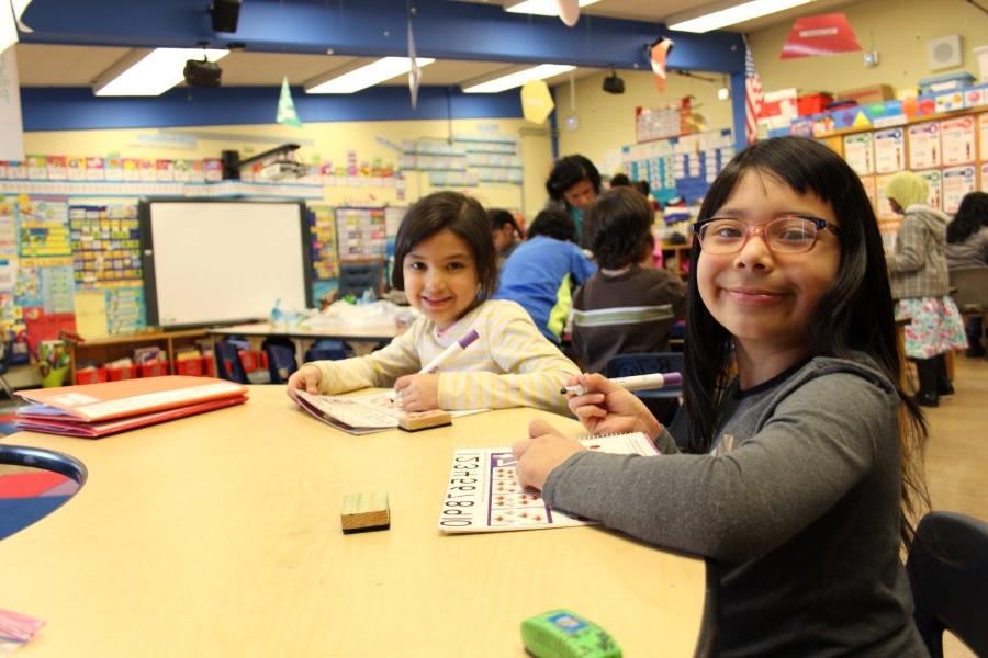 两个学生坐在教室的桌子前微笑着拍照