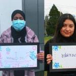 A group of students pose with a hand drawn sign that says welcome in different languages